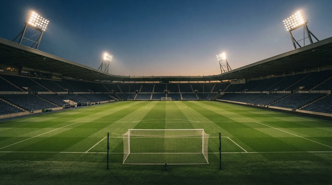 An empty football stadium with floodlight masts at dusk