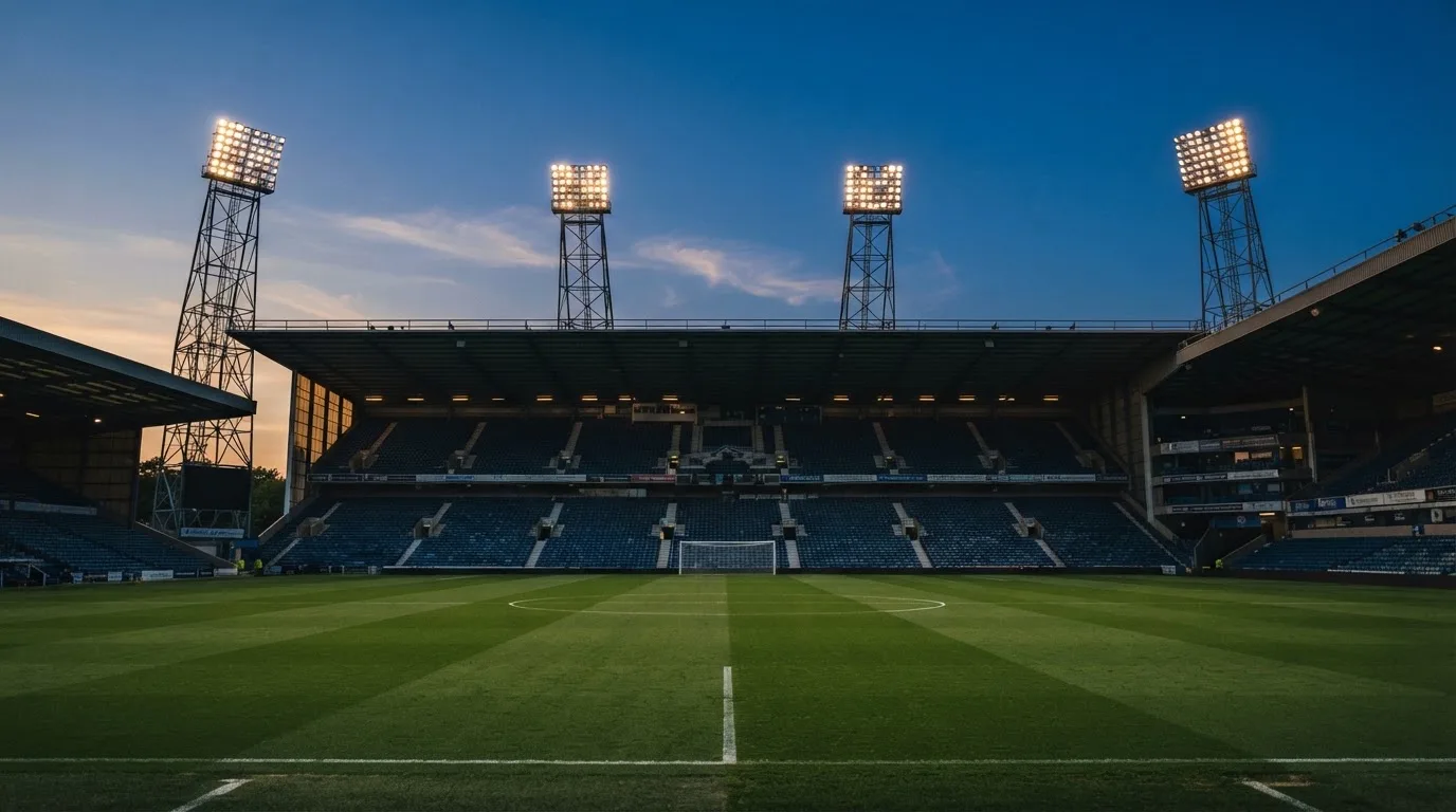 An empty football stadium with floodlight masts at dusk