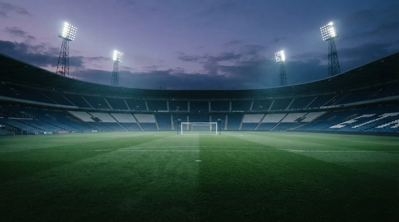 An empty football stadium with floodlight masts at dusk